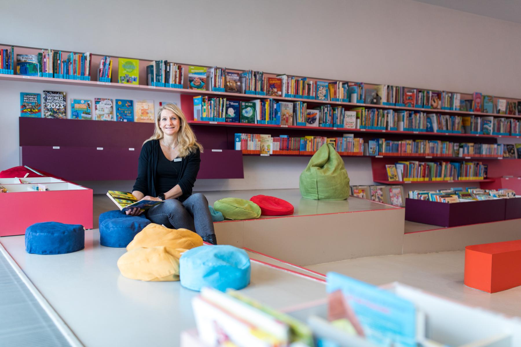 Heike Rosendahl sitzt mit einem Buch in der Kinderbibliothek