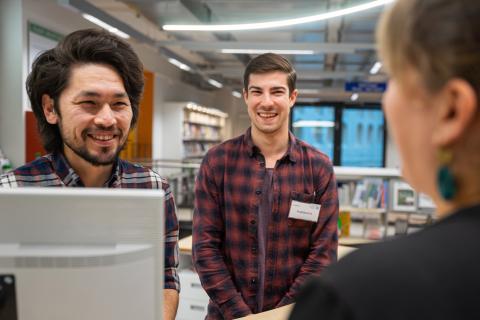 Zwei männliche Bibliotheksmitarbeiter sprechen mit einer Frau in der Bibliothek.