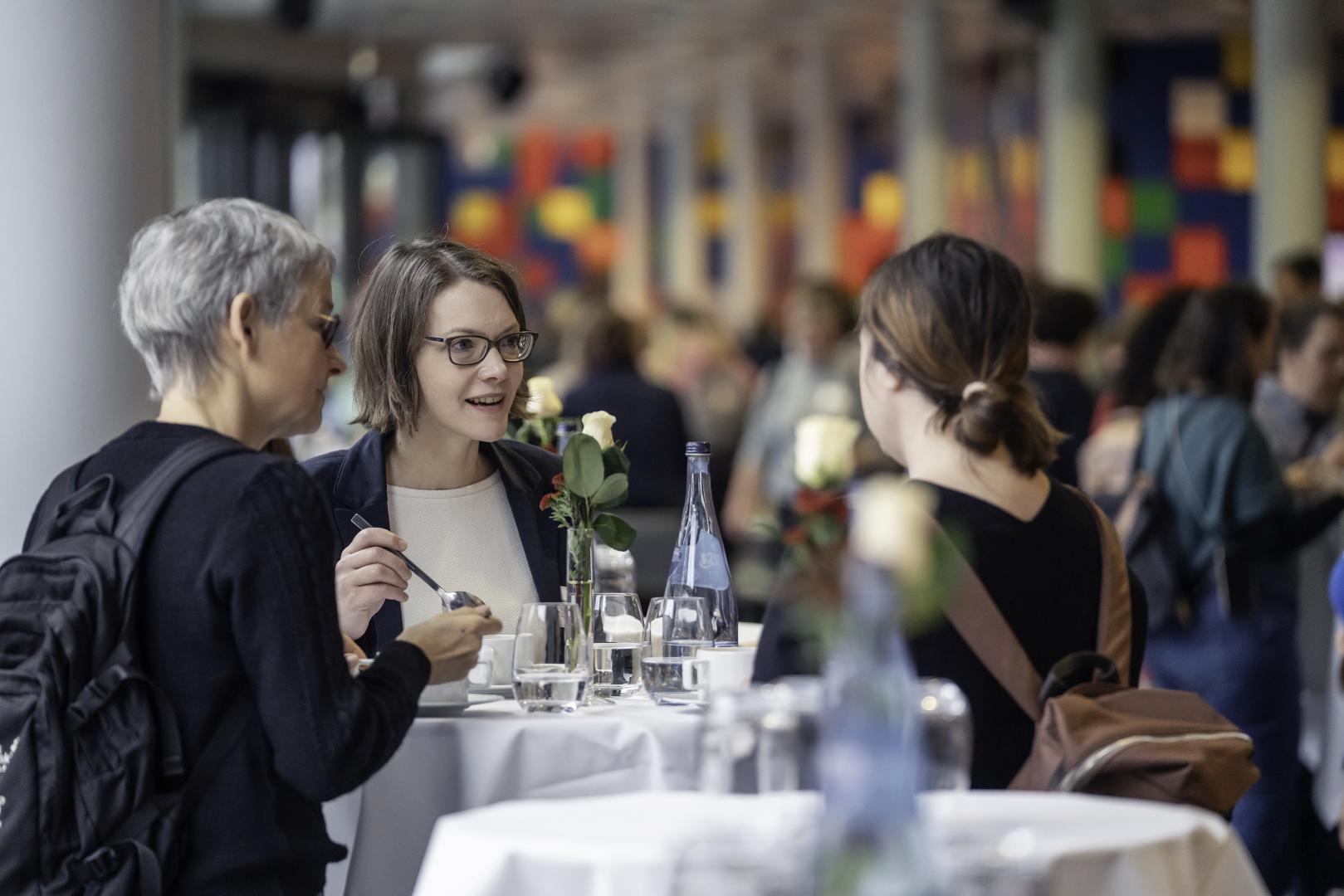 Teilnehmer*innen essen und unterhalten sich am Stehtisch.