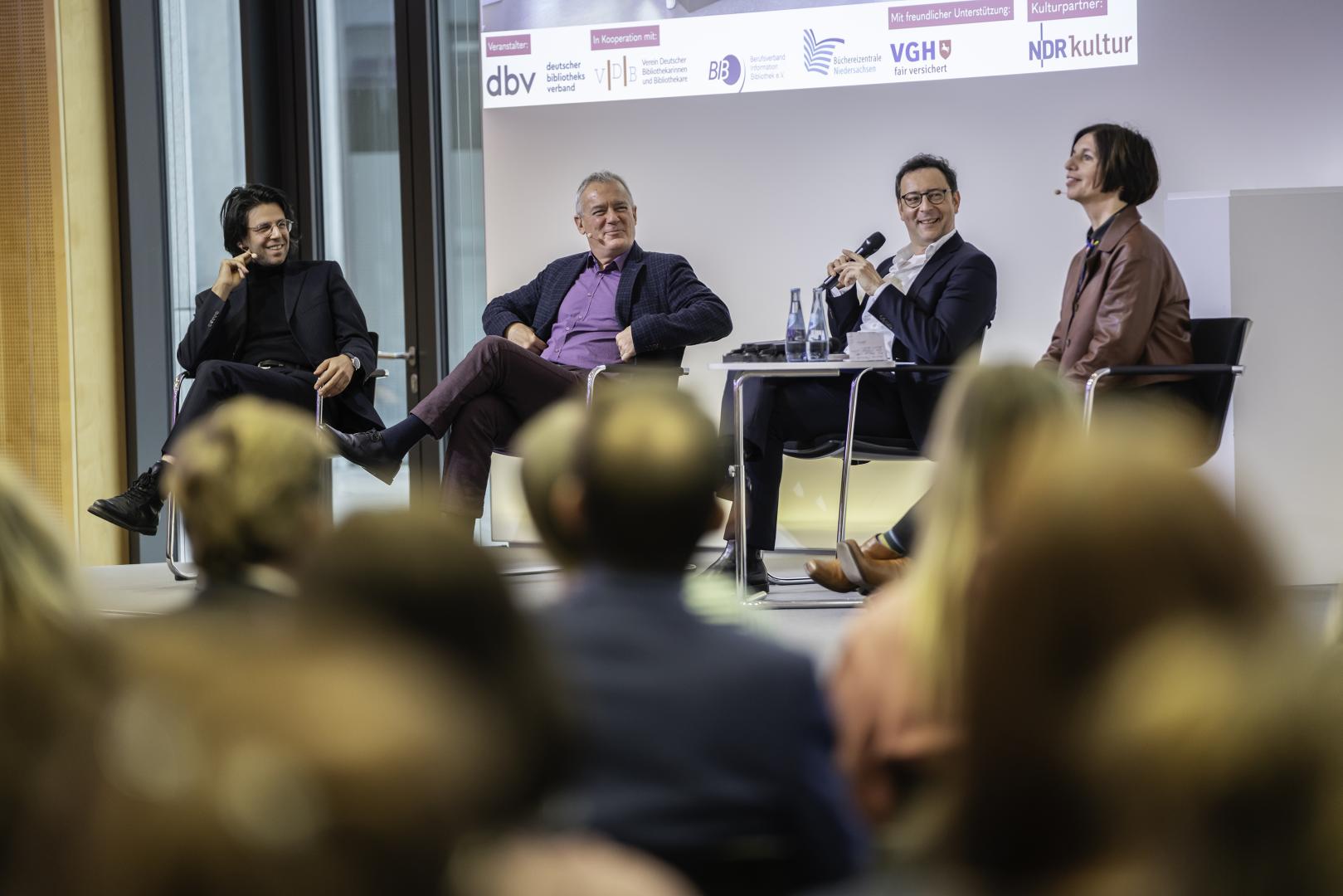 Vier Personen sitzen auf dem Podium und diskutieren.