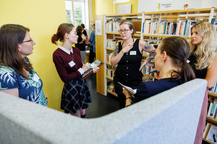 Eine Gruppe Frauen steht in der Bibliothek. Sie unterhalten sich.